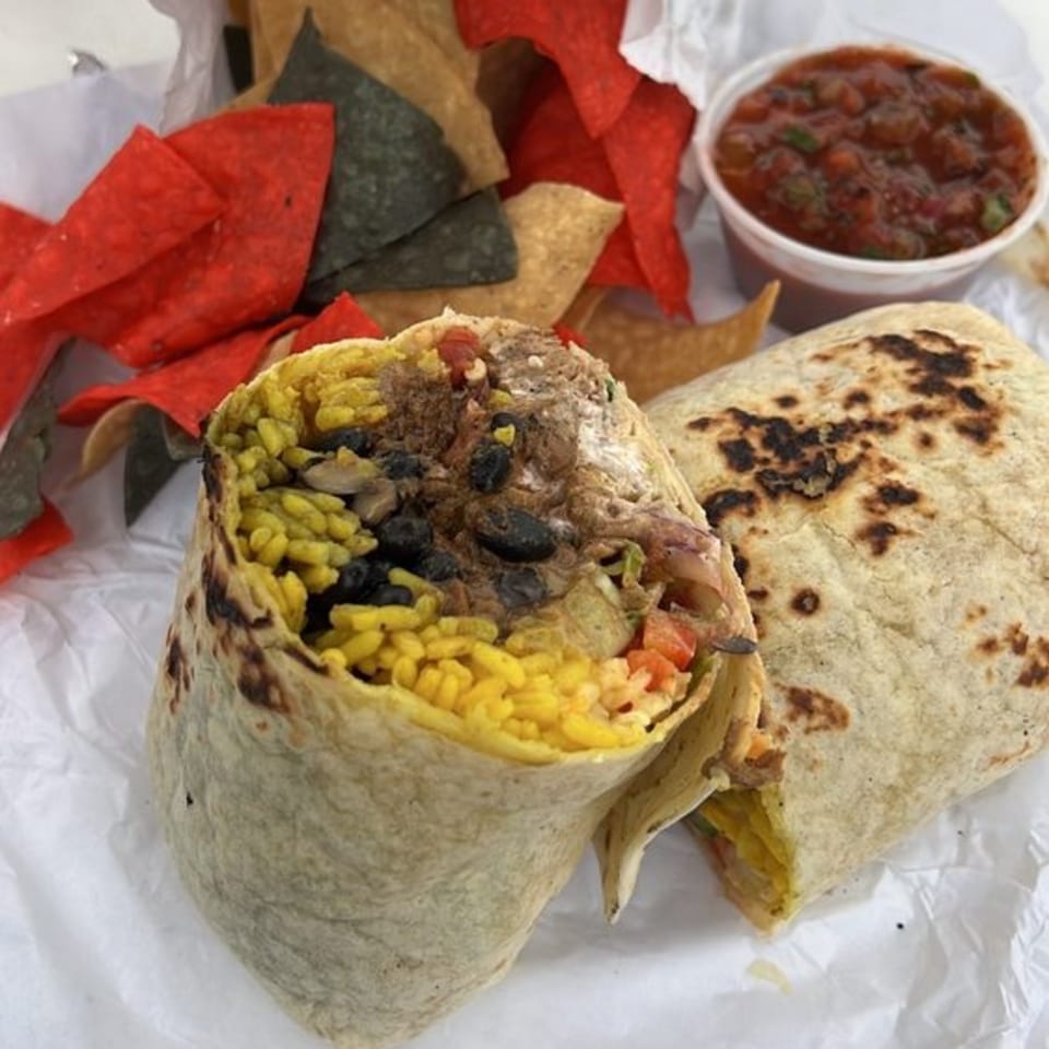 Two burritos, one cut open to show yellow rice and black beans, with chips and salsa.