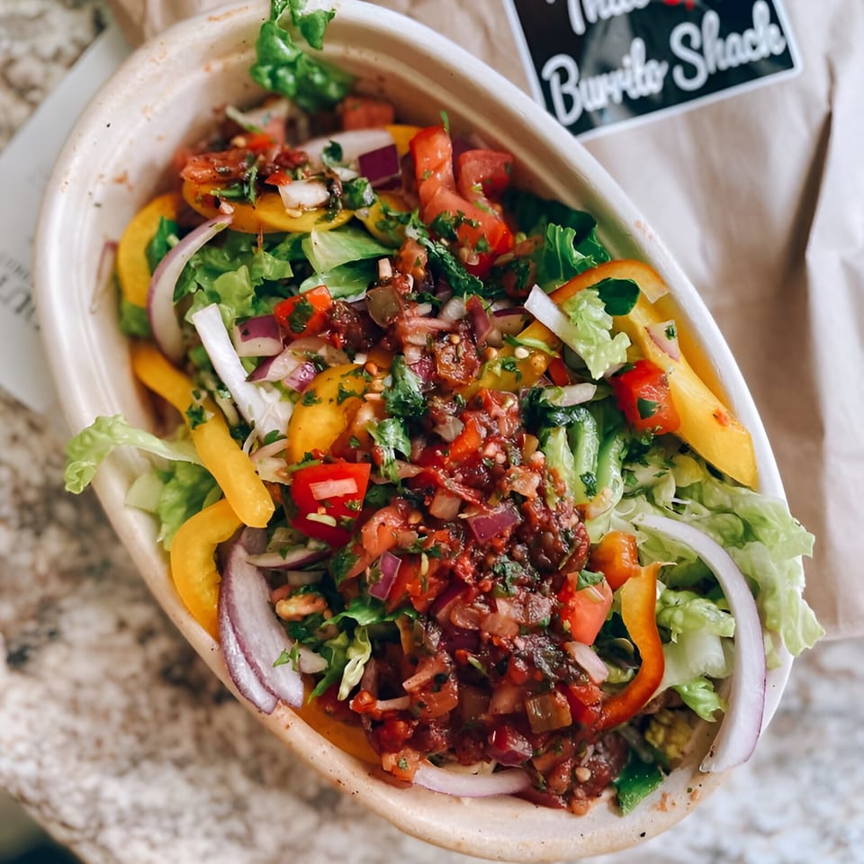 A vibrant burrito bowl from That Epic Burrito Shack, filled with fresh lettuce, peppers, onions, and salsa.