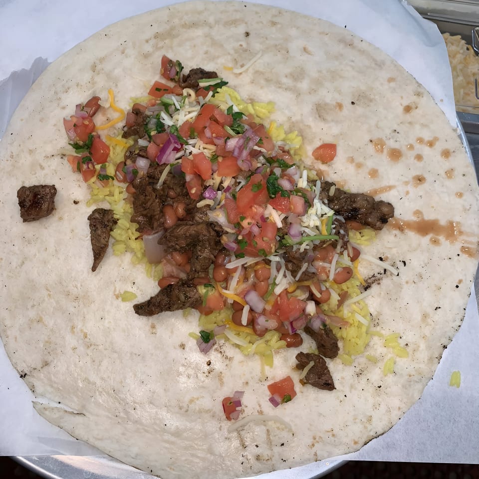 An open burrito from That Epic Burrito Shack, filled with steak, rice, beans, pico de gallo, and cheese.